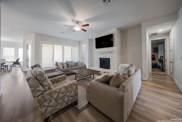 living room with a stone fireplace, visible vents, and light wood-style floors