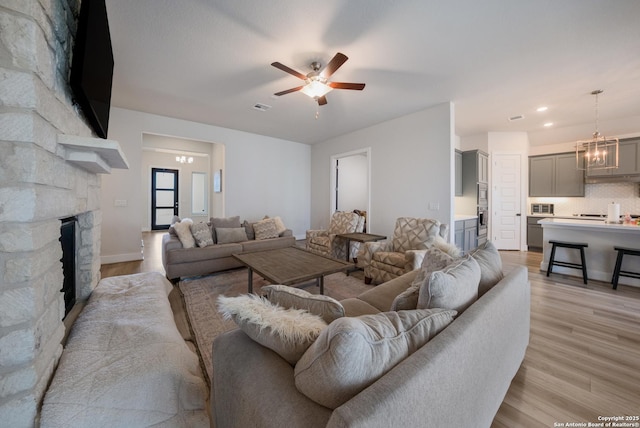 living area with light wood-style flooring, a fireplace, visible vents, and ceiling fan with notable chandelier