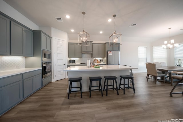 kitchen featuring a large island, appliances with stainless steel finishes, light countertops, and decorative light fixtures