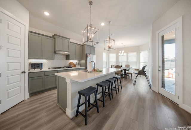 kitchen with a kitchen breakfast bar, light countertops, tasteful backsplash, an island with sink, and pendant lighting