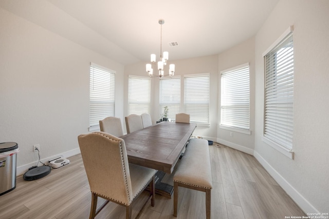 dining space with light wood-type flooring, a healthy amount of sunlight, and a notable chandelier