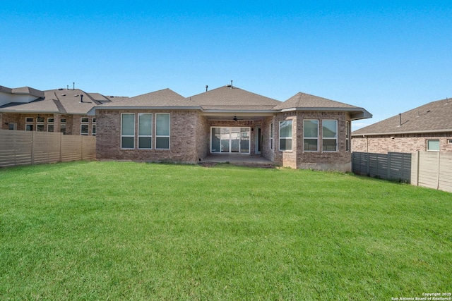 back of property featuring a fenced backyard, a lawn, and brick siding