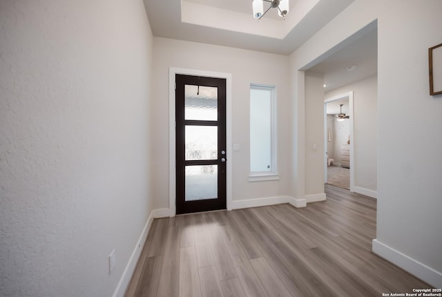 foyer featuring light wood finished floors, baseboards, and a tray ceiling