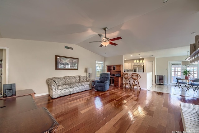 living room featuring lofted ceiling, visible vents, wood finished floors, baseboards, and ceiling fan with notable chandelier