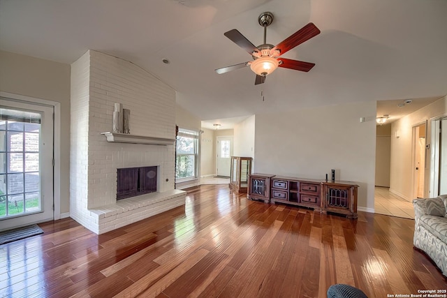 living room featuring baseboards, a ceiling fan, lofted ceiling, wood finished floors, and a brick fireplace