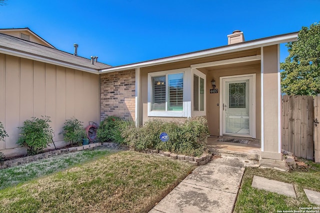 doorway to property featuring a yard, brick siding, fence, and a chimney