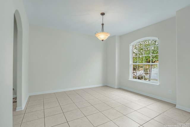 empty room featuring arched walkways, baseboards, and light tile patterned floors