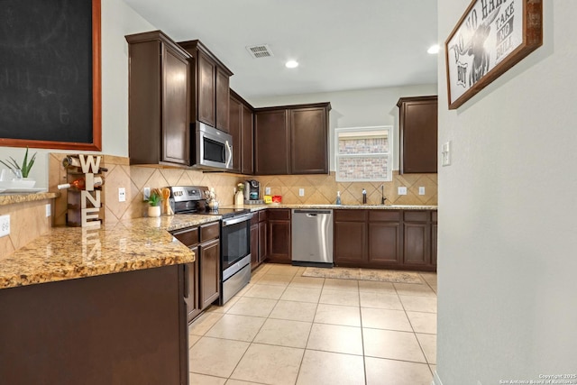 kitchen featuring light stone counters, light tile patterned floors, stainless steel appliances, backsplash, and dark brown cabinets