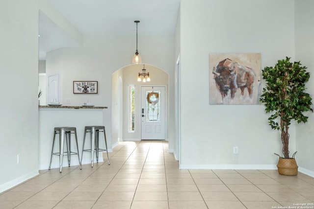 foyer featuring arched walkways, light tile patterned flooring, and baseboards