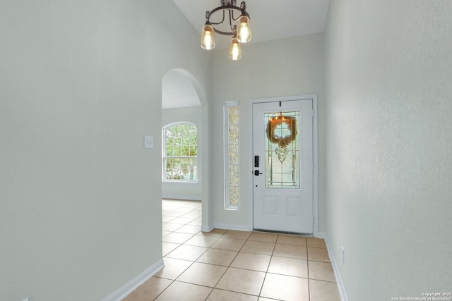 entrance foyer featuring a chandelier, arched walkways, baseboards, and light tile patterned floors