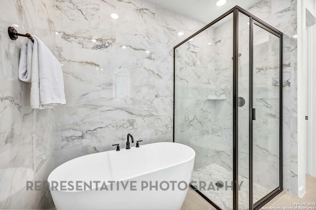 bathroom with tile walls, a freestanding tub, a marble finish shower, and recessed lighting