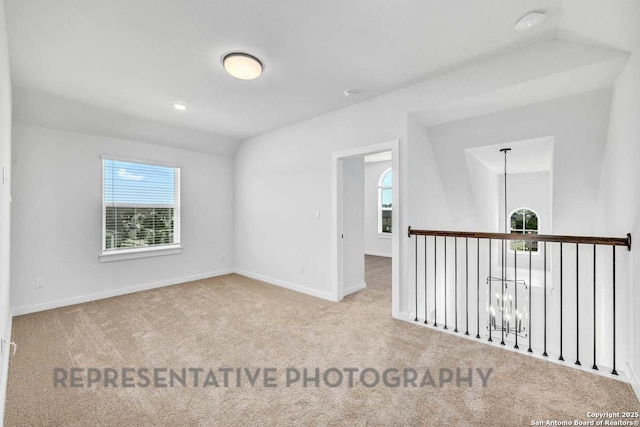 spare room featuring light carpet, a chandelier, and baseboards