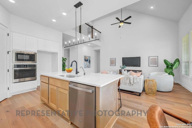 kitchen with decorative light fixtures, stainless steel appliances, open floor plan, light countertops, and a center island with sink