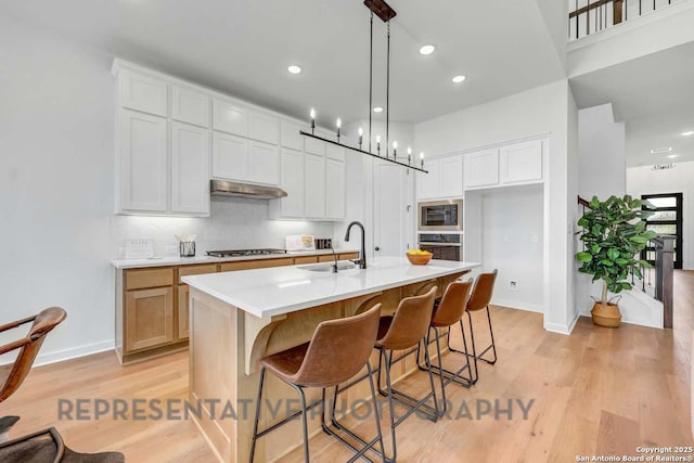 kitchen featuring light countertops, a sink, a kitchen island with sink, and white cabinets