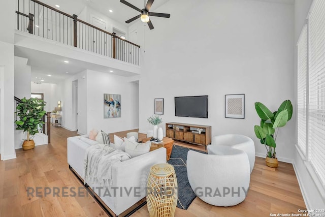 living area with baseboards, a towering ceiling, ceiling fan, wood finished floors, and recessed lighting