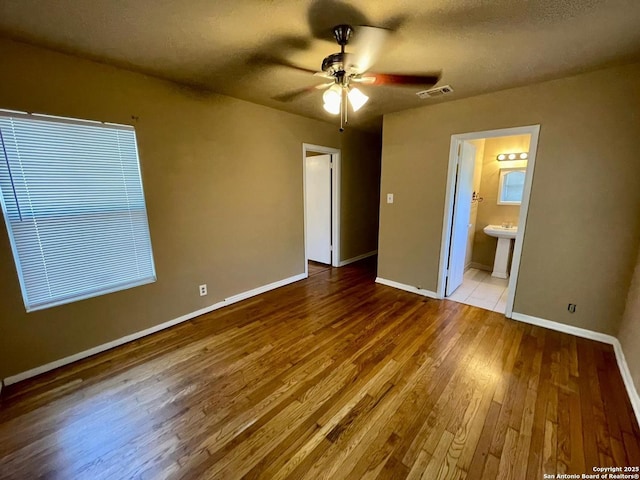 unfurnished bedroom featuring baseboards, visible vents, ensuite bath, wood finished floors, and a textured ceiling