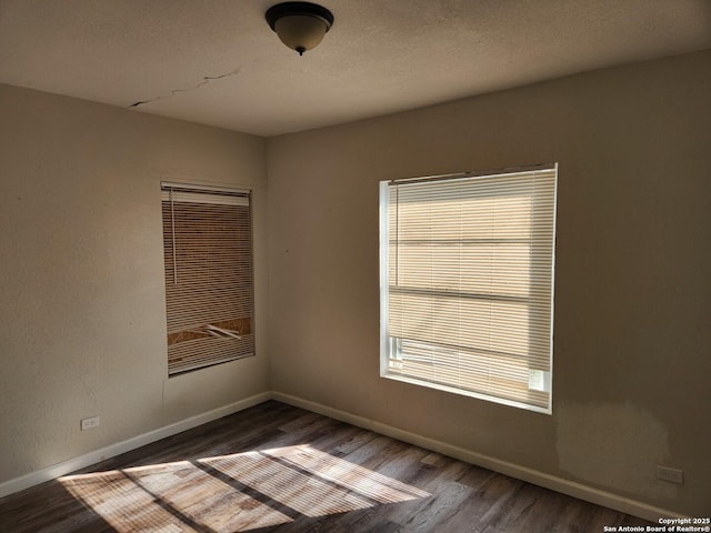 unfurnished room featuring a textured ceiling, dark wood finished floors, and baseboards