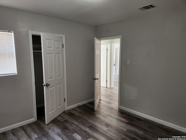 unfurnished bedroom with visible vents, baseboards, and dark wood-type flooring