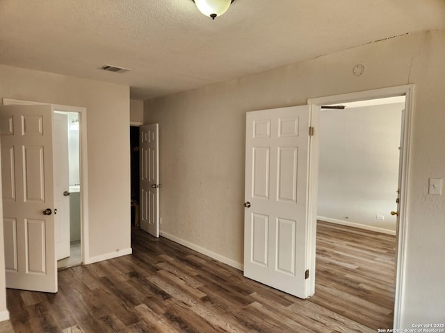 unfurnished bedroom with baseboards, visible vents, dark wood finished floors, and a textured ceiling