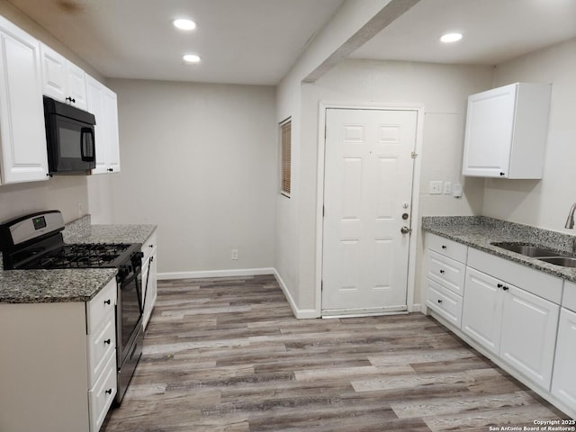 kitchen with white cabinetry, a sink, dark stone countertops, black microwave, and stainless steel gas range oven