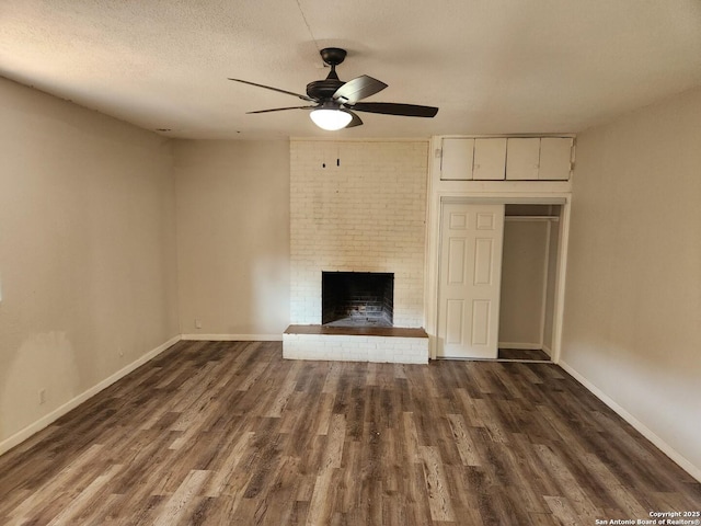 unfurnished living room featuring a textured ceiling, ceiling fan, dark wood-type flooring, baseboards, and a brick fireplace