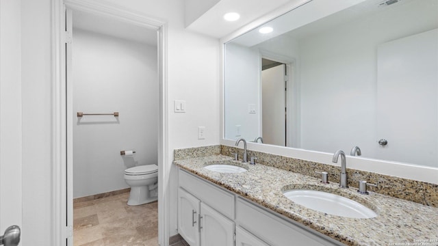 bathroom with double vanity, a sink, toilet, and baseboards