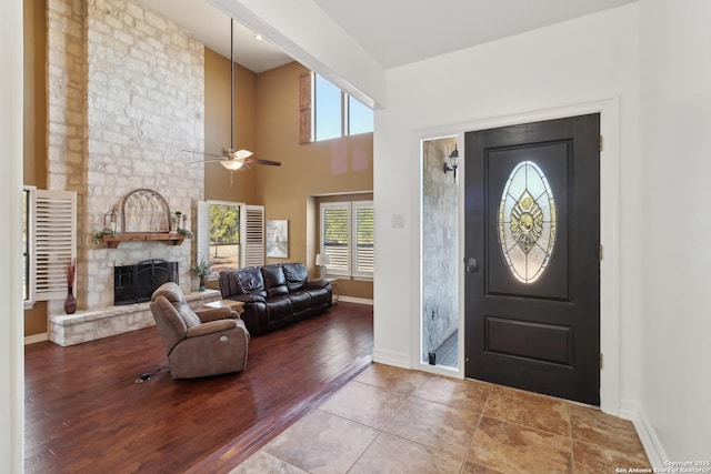 entrance foyer featuring baseboards, ceiling fan, wood finished floors, a high ceiling, and a fireplace