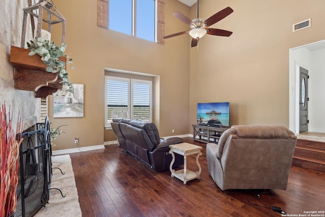 living area with wood-type flooring, visible vents, a fireplace with raised hearth, and baseboards