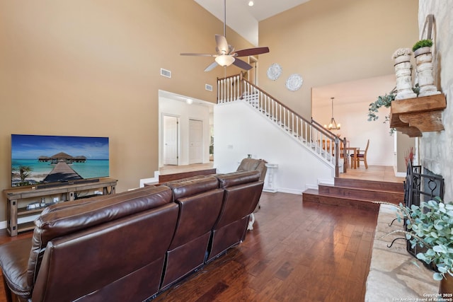 living area with a large fireplace, visible vents, wood-type flooring, stairs, and ceiling fan with notable chandelier