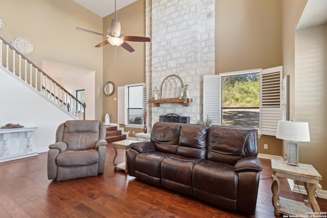 living room with a high ceiling, a fireplace, baseboards, stairway, and wood-type flooring