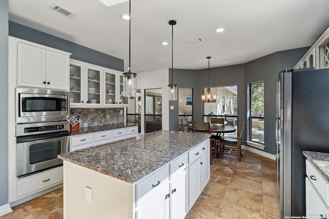 kitchen with a center island, stainless steel appliances, tasteful backsplash, visible vents, and glass insert cabinets