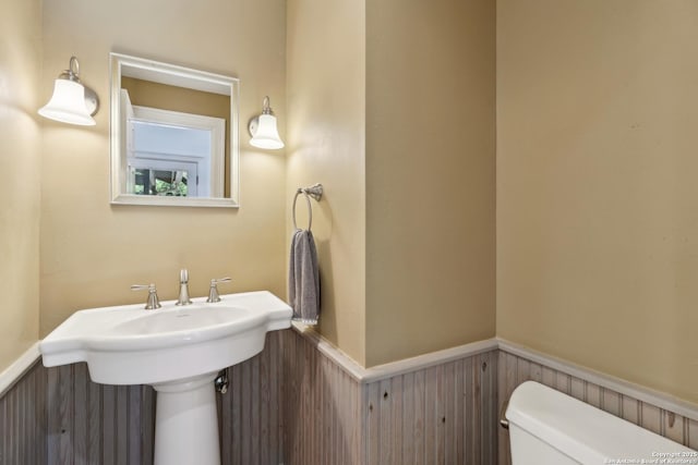 half bath with wainscoting, a sink, and toilet