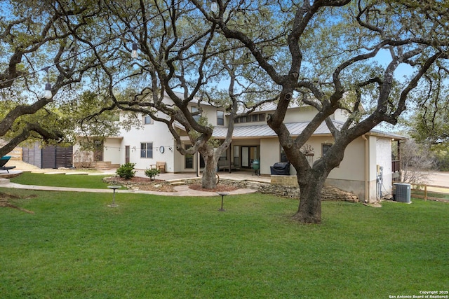 view of front facade with a standing seam roof, a front yard, metal roof, and stucco siding