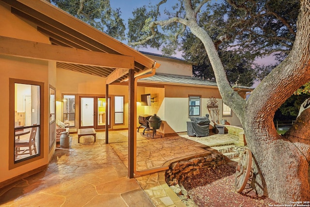 back of property with metal roof, a standing seam roof, a patio area, and stucco siding