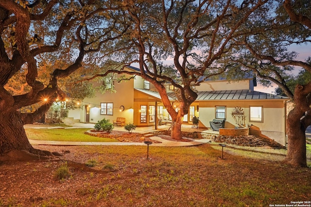 back of property at dusk with a standing seam roof, metal roof, and a lawn