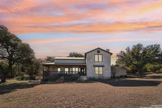 view of front of home with metal roof, covered porch, stone siding, a standing seam roof, and a chimney