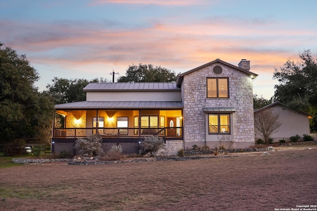 back of house featuring a standing seam roof, covered porch, metal roof, and a chimney