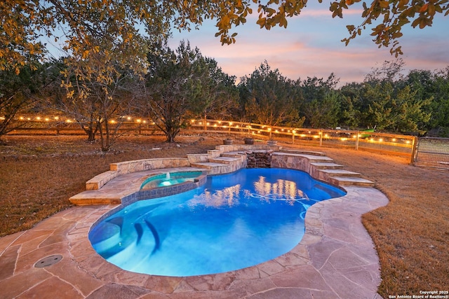 pool at dusk featuring fence and a pool with connected hot tub