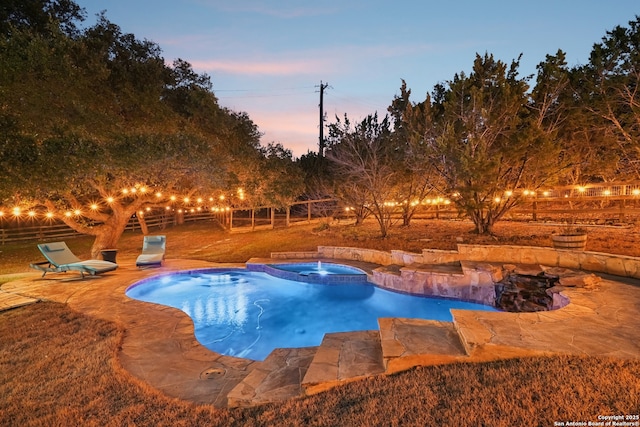 pool at dusk with a pool with connected hot tub, fence, and a patio