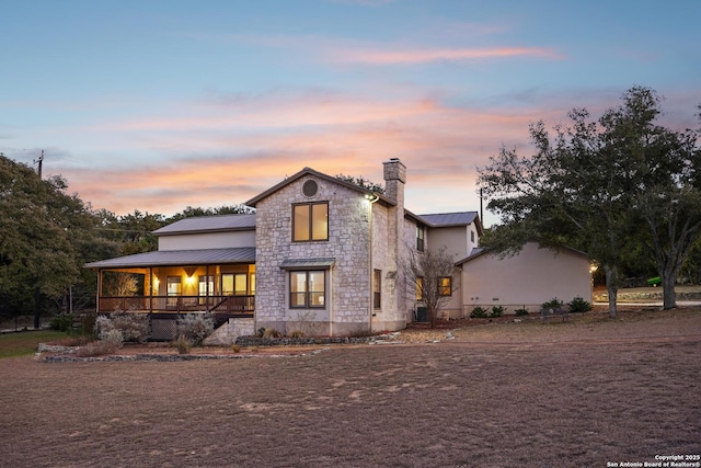 view of front of house with a chimney, covered porch, a standing seam roof, metal roof, and stone siding