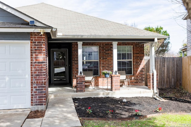 doorway to property with an attached garage, fence, a porch, and brick siding