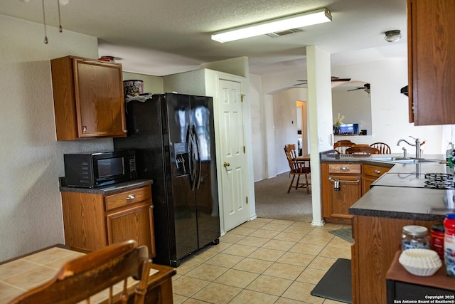 kitchen featuring brown cabinetry, dark countertops, a sink, and black appliances