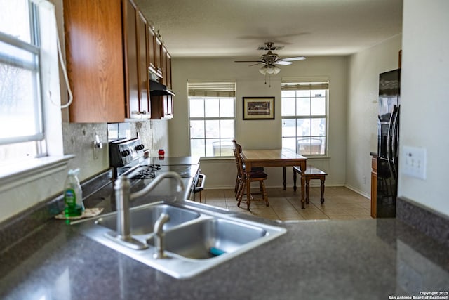 kitchen with under cabinet range hood, electric stove, tasteful backsplash, brown cabinetry, and dark countertops