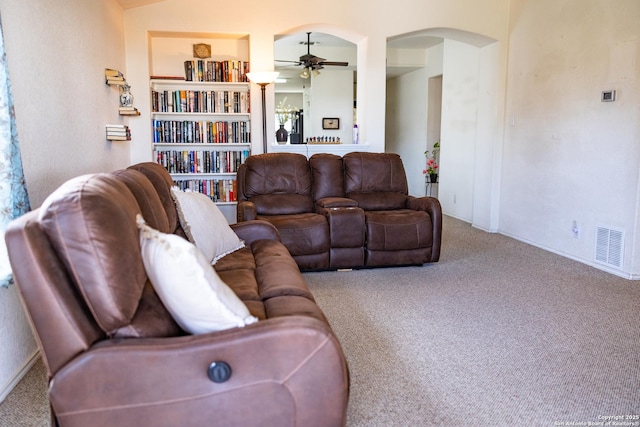 carpeted living room featuring a ceiling fan, arched walkways, visible vents, and built in shelves