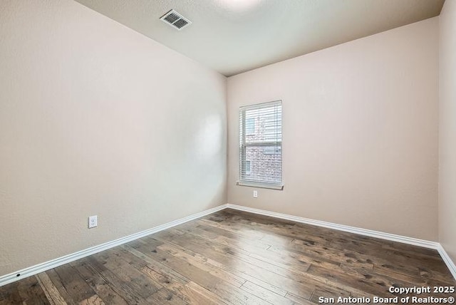 empty room with dark wood-style flooring, visible vents, and baseboards