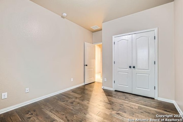 unfurnished bedroom with a closet, dark wood finished floors, visible vents, and baseboards