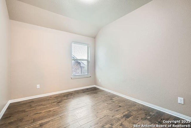 empty room featuring baseboards, vaulted ceiling, and dark wood-type flooring