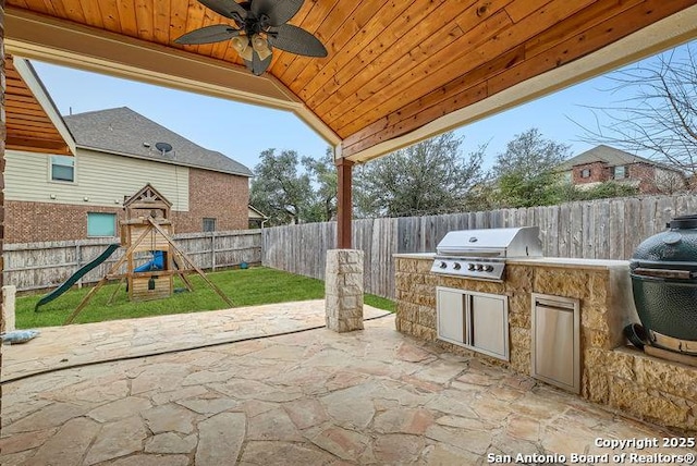 view of patio / terrace featuring an outdoor kitchen, a fenced backyard, a playground, a grill, and a ceiling fan