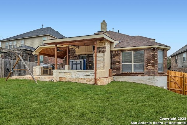 rear view of house with a chimney, fence, a lawn, and brick siding