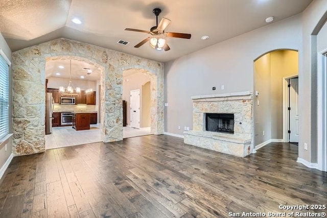 unfurnished living room featuring arched walkways, lofted ceiling, a fireplace, visible vents, and dark wood-style floors